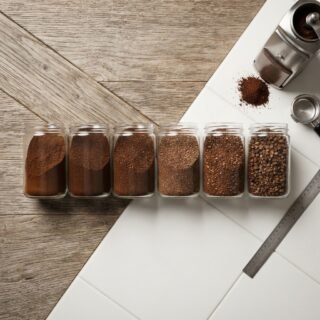 Grind size reference samples in labeled glass jars from fine to coarse, Baratza grinder, lab surface